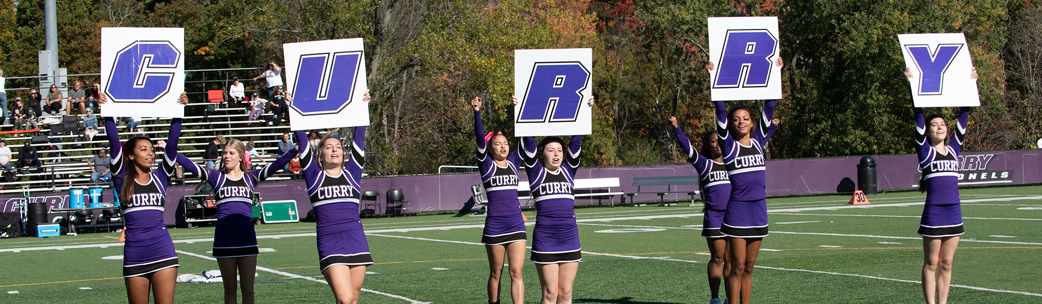 Curry College cheerleaders hold up "Curry" letters at Katz Field during Homecoming and Family Weekend