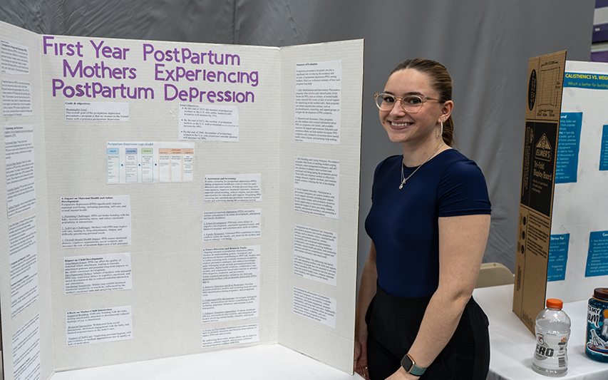 Kendra Aucoin poses next to her poster at the Academic Forum