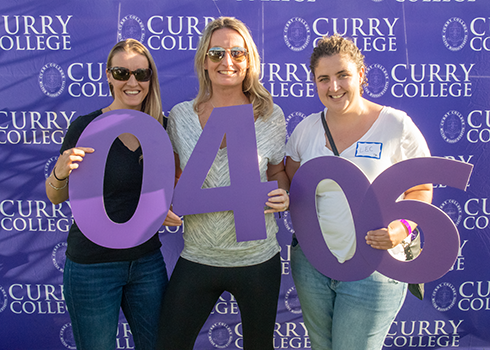 Curry College alumni pose for a photo with their class year numbers