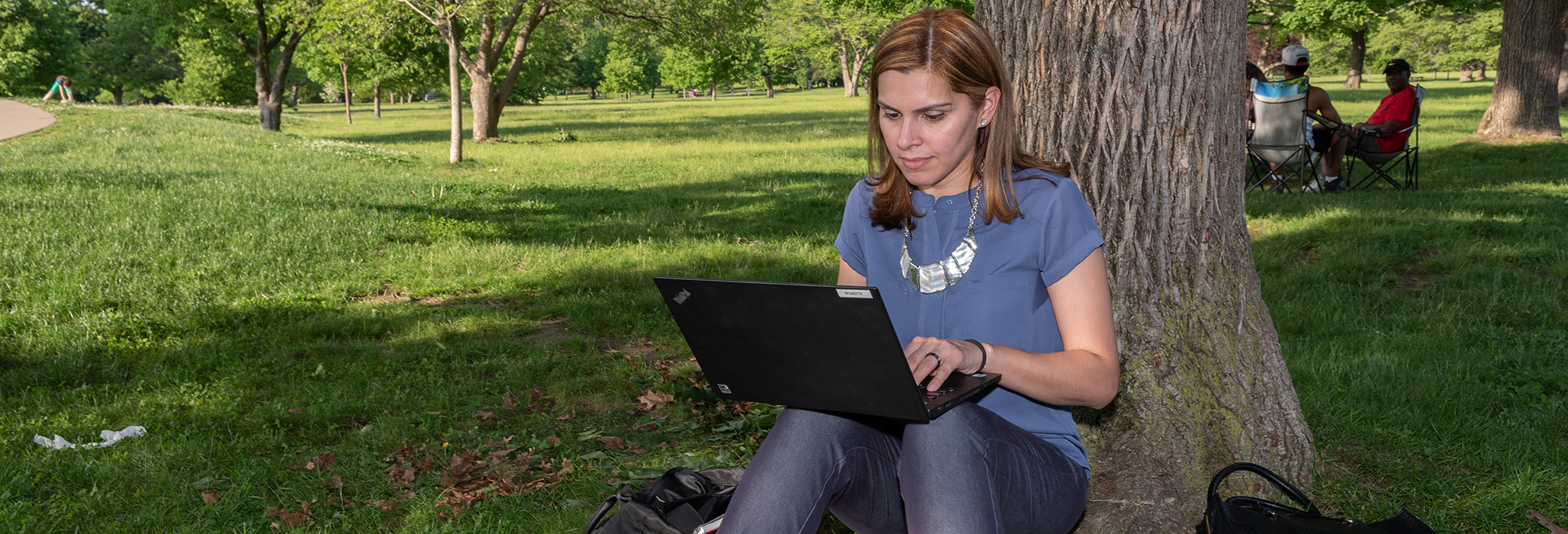 A Curry College graduate student works on her laptop in the park