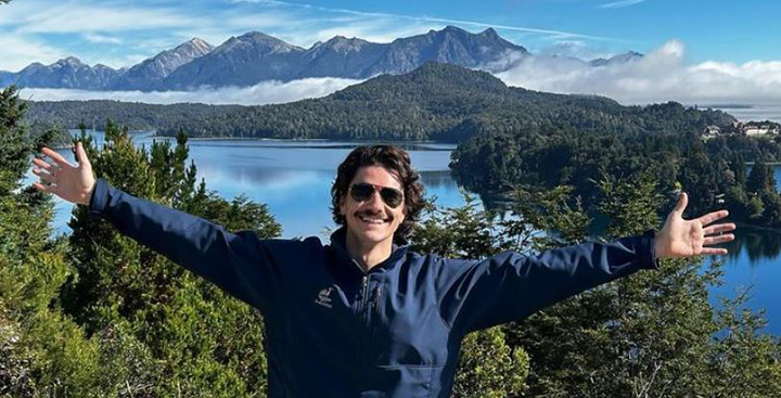 Curry student abroad with arms wide open in front of a mountain lake