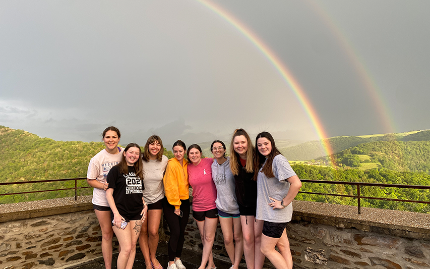 Curry College students abroad pose in front of a double rainbow